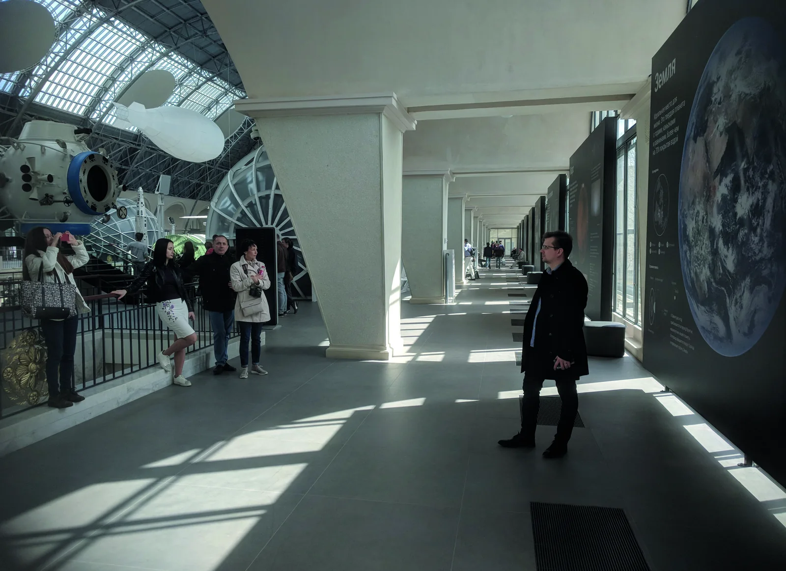 The Cosmonautics and Aviation centre at VDNH: plates along the glass wall, visitors in the sunlit hall