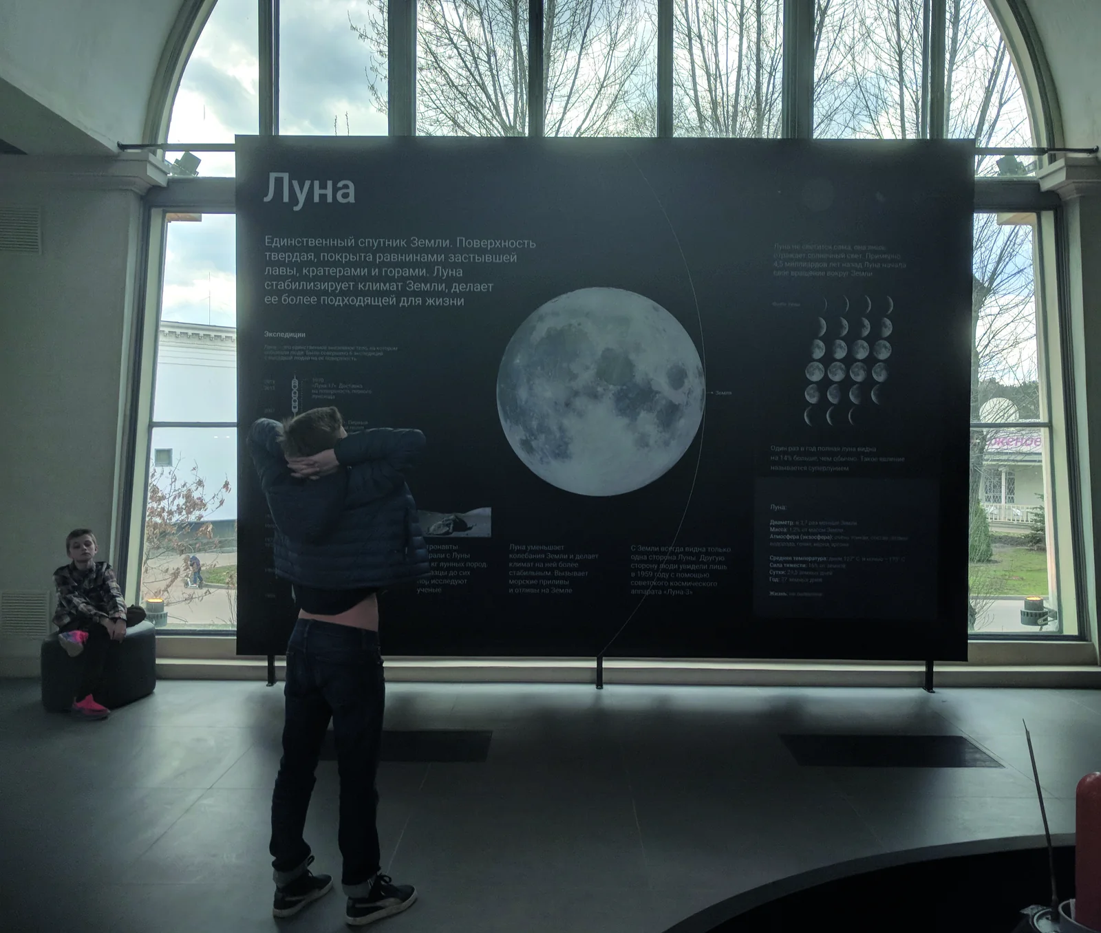 A visitor in front of the Moon plate, a child on a pouf beside it